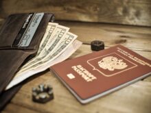 photo of a brown passport beside a wallet with dollar bills